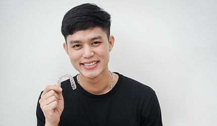 young person holding their Invisalign trays and smiling