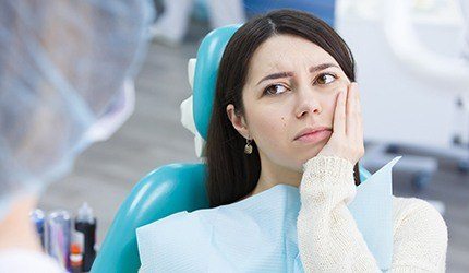 Woman in dental chair holding cheek