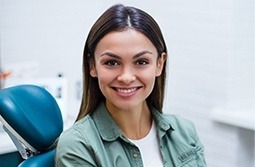 Smiling young woman in dental chair wearing green buttoned shirt