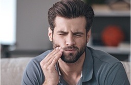 Man sitting on couch holding cheek in pain