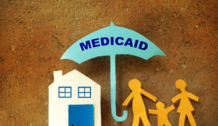 paper cutouts of a house and a family being guarded by an umbrella that says Medicaid
