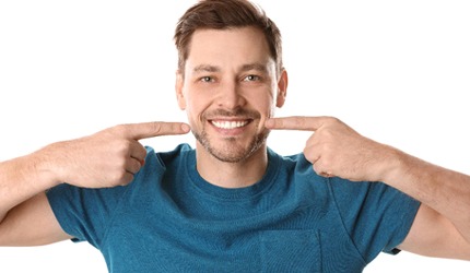 Smiling man points to his porcelain veneers in DeSoto