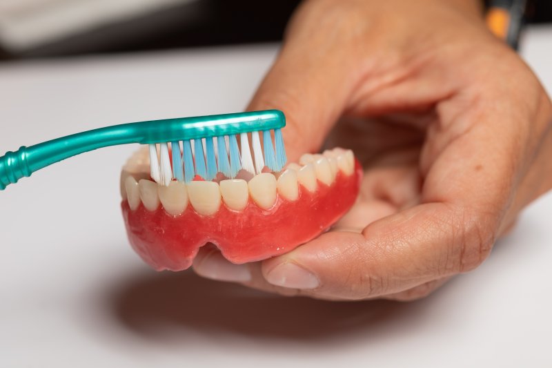 person caring for dentures by brushing them