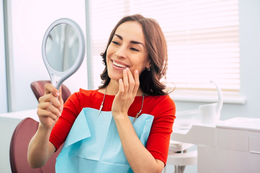 Woman in orange shirt in dental office admiring reflection in mirror