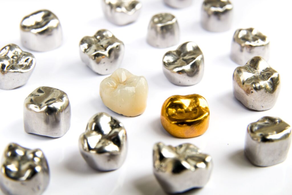 A tooth-colored dental crown among many metallic ones on a white surface
