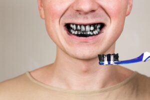 Person brushing their teeth with charcoal toothpaste.